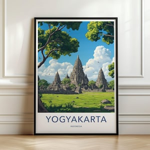 Puede incluir: Un póster de viaje enmarcado que muestra el complejo de templos de Prambanan en Yogyakarta, Indonesia. La ilustración muestra templos de piedra bajo un cielo azul brillante con nubes blancas, rodeados de hierba verde y árboles. El texto dice YOGYAKARTA INDONESIA.