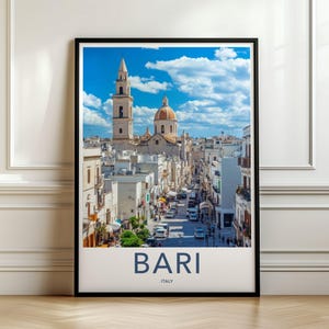 以下が含まれることがあります： イタリアのバーリの晴れた街並みが描かれた、額装された縦型のウォールアートプリント。高い鐘楼、大きなドーム、白い建物が、雲のある明るい青空の下に写っています。下部には「BARI ITALY」という文字が印刷されています。