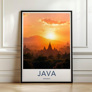 以下が含まれることがあります： インドネシアのジャワ島の夕景を描いた額入りアートプリント。オレンジ色の空を背景に、寺院の尖塔と山のシルエットが浮かび上がっています。下部の白い枠には、大きな青い文字で「JAVA」、その下に「INDONESIA」と記されています。