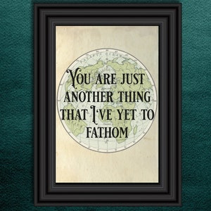 May include: A framed print with a black frame, featuring a vintage-style world map. The map is centered and has the text "You are just another thing that I've yet to fathom" in a serif font. The background is a textured teal.