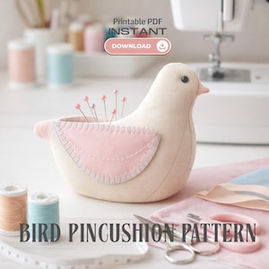 Può includere: Un cuscino a forma di uccello beige con un dettaglio alare rosa, che contiene spilli con capocchie rosa. L'immagine include anche rocchetti di filo, forbici e il testo "BIRD PINCUSHION PATTERN". Il design è per un PDF stampabile.