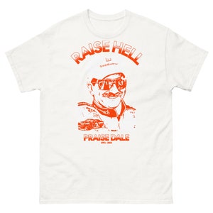 May include: White t-shirt with an orange print of a race car driver with the text "Raise Hell" and "Praise Dale 1951-2001".