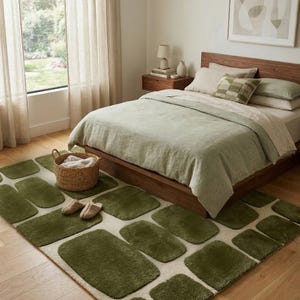 Könnte beinhalten: Ein Schlafzimmer mit einem Bett mit salbeigrünem Bettzeug und einem gemusterten Teppich. Der Teppich hat einen cremefarbenen Hintergrund mit olivgrünen rechteckigen Formen. Ein Weidenkorb und Hausschuhe liegen auf dem Teppich.