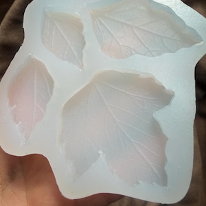 Può includere: Uno stampo in silicone trasparente e flessibile con quattro forme di foglie, che mostrano dettagli intricati delle venature. Lo stampo è per l'artigianato, con una superficie liscia e un aspetto traslucido. Le foglie sono di diverse dimensioni.