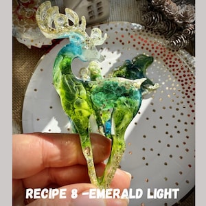 Op de afbeelding: Een decoratief hars hert figuur met smaragdgroene, blauwe en gouden glitter accenten. De tekst "RECIPE 8 - EMERALD LIGHT MARBLE" staat onderaan. Het hert wordt in een hand gehouden.