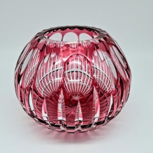 Peut inclure: Un vase rond en verre rouge rubis avec un motif taillé. Le vase a une large ouverture et un design texturé détaillé. Le verre taillé crée un jeu d'ombre et de lumière, rehaussant son attrait décoratif. Un élément de décoration intérieure saisissant.