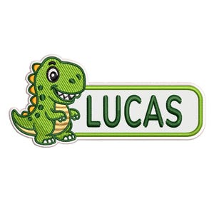 Puede incluir: Parche bordado con un dinosaurio verde de dibujos animados con detalles amarillos. El dinosaurio sonríe junto a un rectángulo blanco con el nombre "LUCAS" en letras verdes. El parche tiene un borde verde.