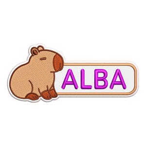 Puede incluir: Un parche bordado que muestra un capibara de color tostado con detalles en marrón junto a una etiqueta rectangular blanca con borde tostado. La etiqueta muestra el nombre ALBA en letras mayúsculas de color morado brillante con textura gruesa.