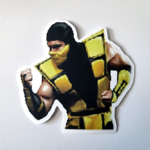May include: A yellow and black pixelated sticker of a video game character. The character is wearing a yellow and black suit and a black mask. The character is in a fighting pose.