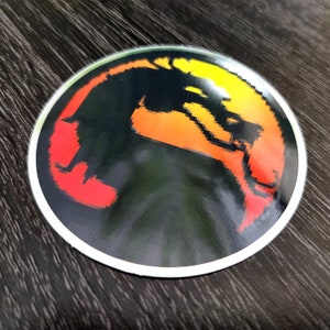 May include: A round sticker with a pixelated image of a black dragon silhouette against a red, orange, and yellow background.