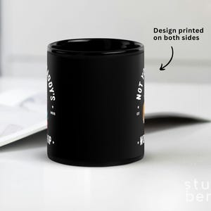May include: Black ceramic mug with white text that reads "NOT YOUR BODYS WORKSHOP" and "S.A.D.Y'S". The design is printed on both sides. The mug is on a white surface.