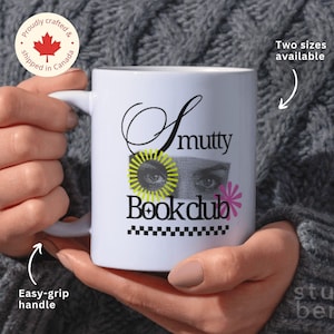 Puede incluir: Taza de cerámica blanca con un diseño en blanco y negro que dice "Smutty Bookclub". El diseño presenta un par de ojos con acentos amarillos y negros y una flor rosa.