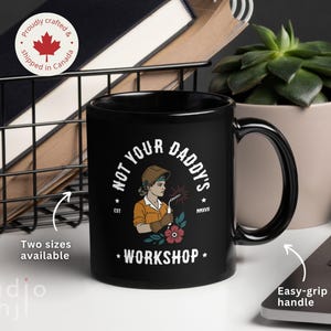 May include: Black ceramic mug with the text "NOT YOUR DADDY'S WORKSHOP" and an illustration of a female welder. The mug has an easy-grip handle and is available in two sizes. The mug is proudly crafted and shipped from Canada.