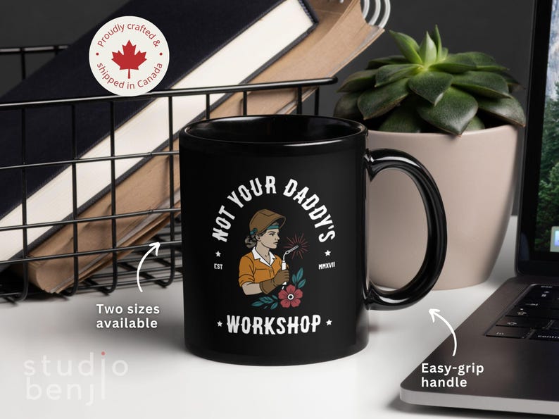 May include: Black ceramic mug with the text "NOT YOUR DADDY'S WORKSHOP" and an illustration of a female welder. The mug has an easy-grip handle and is available in two sizes. The mug is proudly crafted and shipped from Canada.