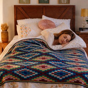 Peut inclure: Un lit avec une tête de lit en bois foncé, des oreillers blancs et une couverture à motifs colorés. La couverture présente un motif géométrique dans les tons de bleu, rouge, jaune et vert. Une personne dort sous la couverture.