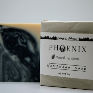 May include: Two bars of handmade soap. One bar has a black and white marbled design. The other bar is wrapped in paper with a label that reads "Forest Musk PHOENIX Natural Ingredients Handmade Soap" and weighs 5.1 oz.