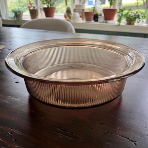 May include: A clear glass pie plate with a fluted edge. The plate is a pale pink color and has a vintage look.