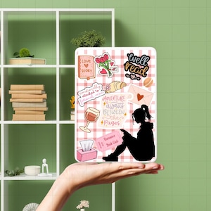 May include: A white and pink checkered tablet case with various stickers, including a silhouette of a person reading, a wine glass, and the words "Adventure awaits between the pages."