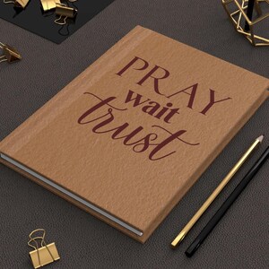 May include: A brown leather journal with the words "PRAY wait trust" printed in maroon on the front cover.
