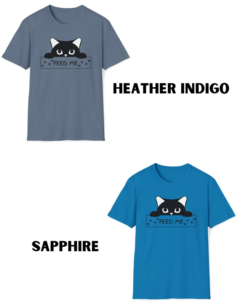 May include: Two t-shirts with a black cat peeking over a sign that says "Feed Me". The t-shirt on the left is heather indigo and the t-shirt on the right is sapphire.