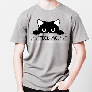 May include: A gray t-shirt with a black cat peeking over a sign that says "FEED ME". The sign has paw prints on either side.