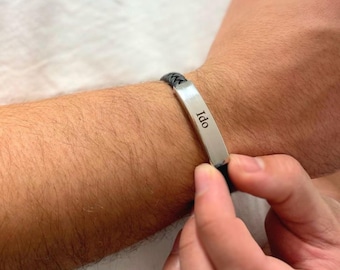 May include: A black leather bracelet with a silver bar that says "Ido" on it.