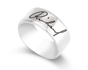 Puede incluir: Un anillo de banda de plata con una firma grabada en negro que dice "Anthony".