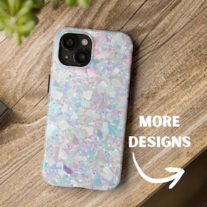May include: A smartphone case with a shimmering, iridescent design. The case features a mosaic pattern of pastel colors, including blue, purple, and white. The text "MORE DESIGNS" is displayed with a white arrow pointing towards the right.