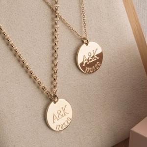May include: Two gold necklaces with round pendants. The pendants are engraved with the initials "A&K" and the date "17.07.20".