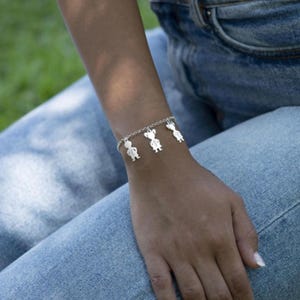 May include: A silver charm bracelet with multiple small silver charms shaped like people. The bracelet is on a person's wrist.