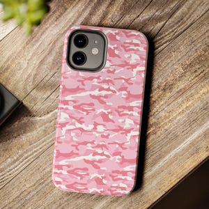 Puede incluir: Funda de teléfono de camuflaje rosa con un recorte para el objetivo de la cámara negro.