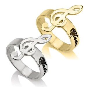 May include: Two rings, one gold-toned and one silver-toned, each featuring a treble clef design. The gold ring has a polished finish, while the silver ring has a matte appearance. Both rings have the word "Music" engraved on the band.