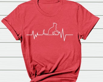 Può includere: Maglietta rossa con un contorno bianco di un gatto all'interno di un grafico del battito cardiaco.