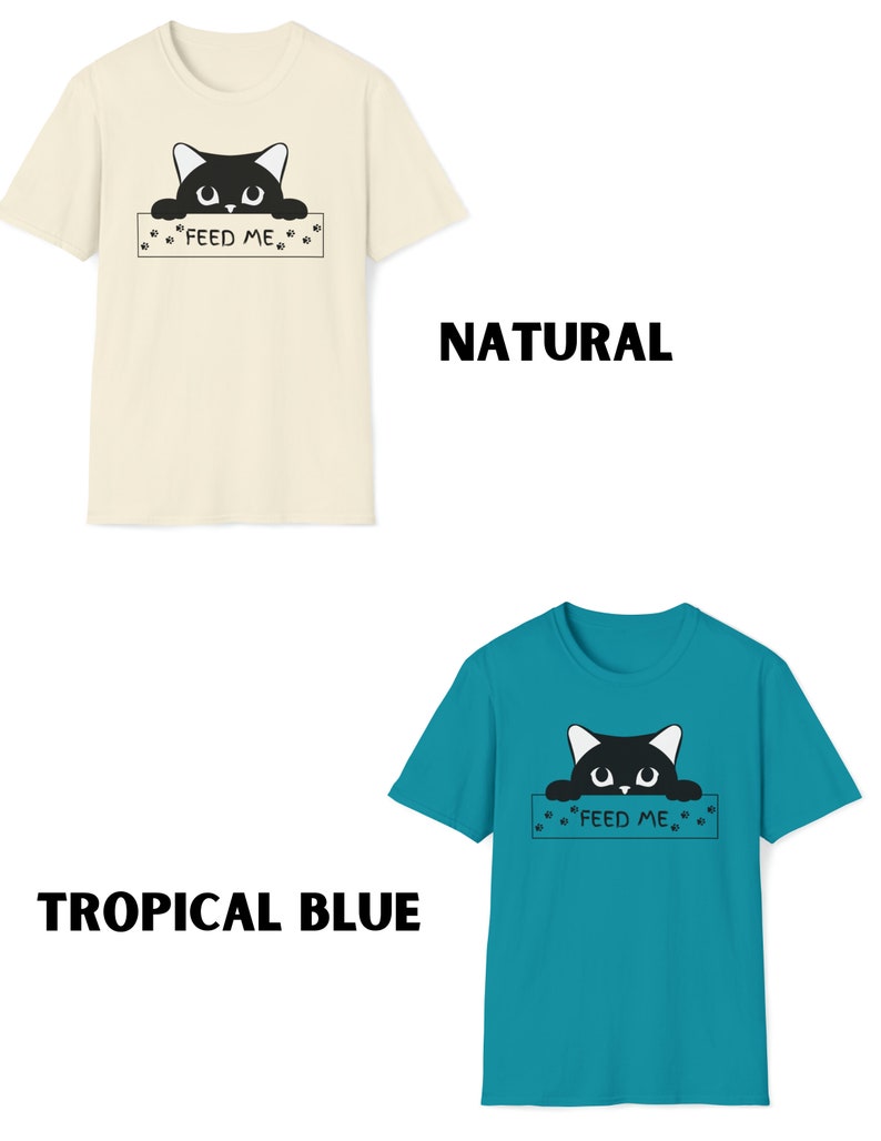 May include: Two t-shirts with a black cat peeking over a sign that says "Feed Me". The t-shirt on the left is a natural color and the t-shirt on the right is tropical blue.