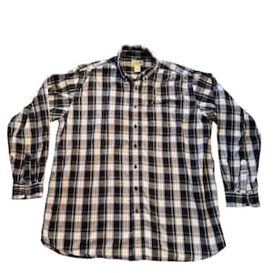 May include: A long-sleeved button-down shirt with a plaid pattern in black, white, and yellow. The shirt has a button-down collar, a chest pocket, and buttoned cuffs. The shirt is made of a soft, woven fabric.