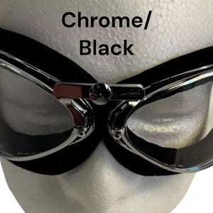 Puede incluir: Gafas de estilo aviador cromadas y negras con lentes transparentes. Las gafas tienen una correa de cuero negra y un marco de metal.