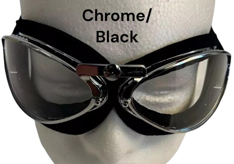 Puede incluir: Gafas de estilo aviador cromadas y negras con lentes transparentes. Las gafas tienen una correa de cuero negra y un marco de metal.