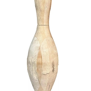 Puede incluir: Un solo bolo de madera sin terminar. El bolo es de color marrón claro con vetas de madera visibles y una textura ligeramente rugosa. El bolo tiene una forma clásica, con un cuerpo redondeado y un cuello y cabeza más estrechos.