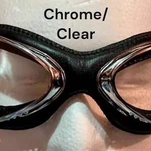 Puede incluir: Gafas de estilo aviador cromadas y transparentes con una correa de cuero negro.