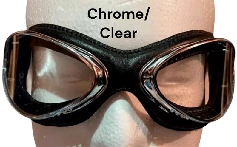 Puede incluir: Gafas de estilo aviador cromadas y transparentes con una correa de cuero negro.