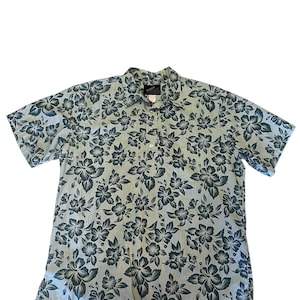 May include: A short-sleeved button-down shirt with a floral pattern. The shirt features a light blue background with a dark teal floral design. The shirt has a collar and a button-up front.