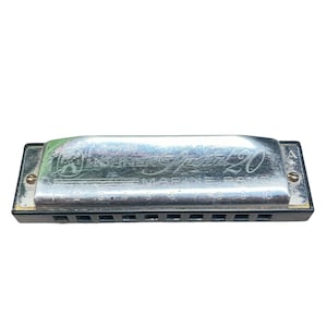 May include: A silver Hohner Marine Band harmonica with black comb and metal covers. The harmonica has the text "Hohner Marine Band 20" engraved on the top cover. The harmonica has 10 holes and is a musical instrument.