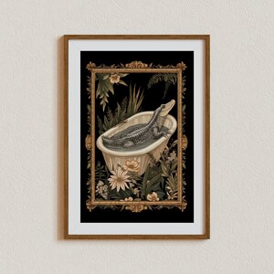Op de afbeelding: Een ingelijste kunstdruk met een alligator die ontspant in een vintage badkuip. Het kunstwerk is omgeven door weelderig groen en bloemen, tegen een zwarte achtergrond. De lijst heeft een warme bruine kleur, wat bijdraagt aan de vintage esthetiek.