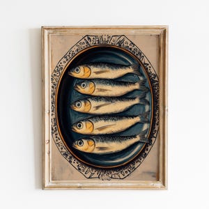 May include: A framed print of a painting depicting five sardines on a blue and white plate. The plate is decorated with a gold rim and a pattern of black and white lines.