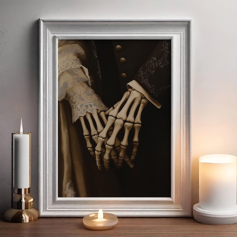 May include: A framed artwork showing two skeletal hands clasped together against a dark backdrop. The hands are intricately detailed, with visible bones. The white frame surrounds the artwork, which is displayed on a wooden surface with candles.