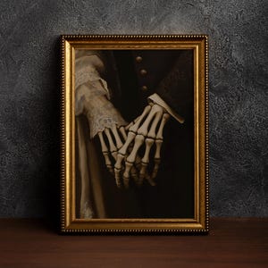 May include: A framed artwork showing a skeletal hand holding a human hand. The gold frame surrounds a dark, gothic image. The human hand is wearing a white lace sleeve, creating a contrast.