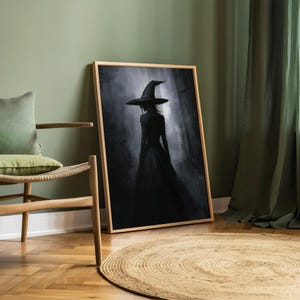 May include: A framed black and white illustration of a witch wearing a pointed hat and a long dress, standing in a dark forest. The image is set against a green wall and a wooden floor.