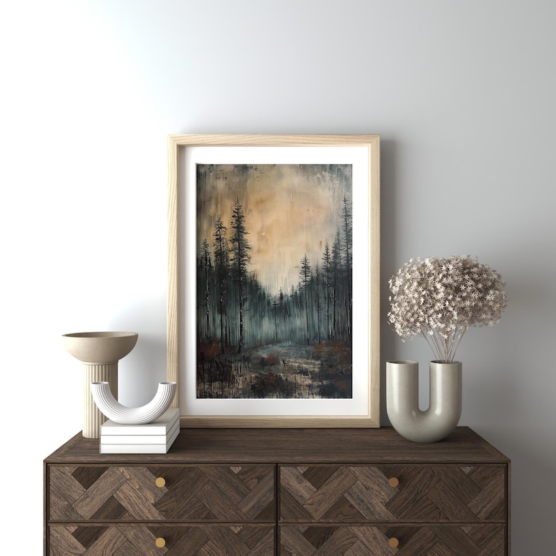 May include: A framed painting of a forest scene with tall, dark trees and a misty background. The sky is a soft orange and yellow, creating a warm and inviting atmosphere.