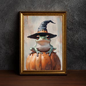 May include: A framed painting featuring a green frog in a black witch's hat with a gold buckle, sitting on an orange pumpkin. The artwork is in a gold frame, set against a dark backdrop, perfect for Halloween.