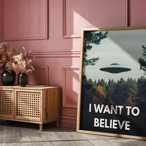 May include: A framed poster with a black and white image of a flying saucer over a forest. The poster has the text "I WANT TO BELIEVE" in white letters.